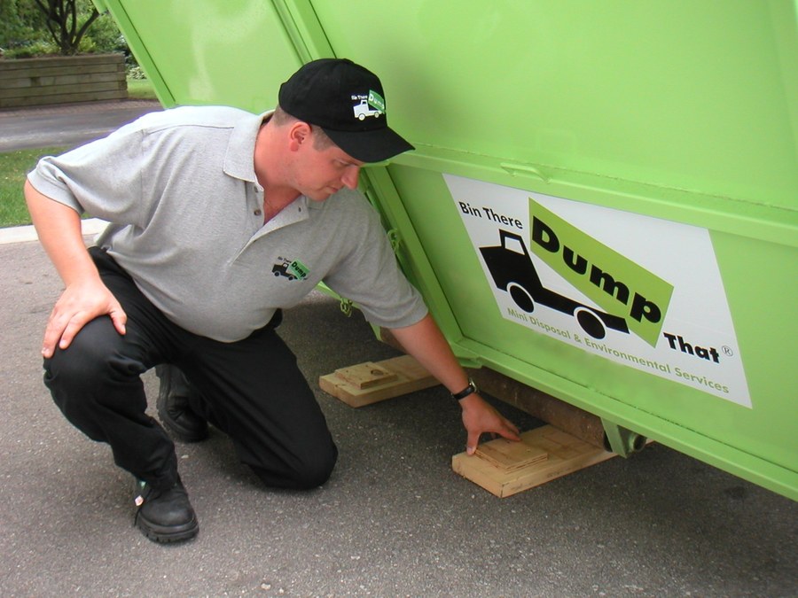 Bin There Dump That driver placing protective boards under a dumpster